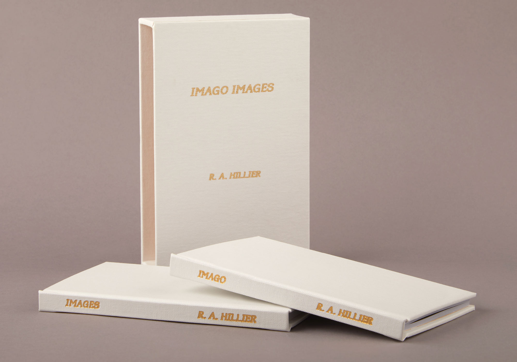 Photograph of the book standing up from front on, shows a white cover and gold foiled text on the cover saying ‘Imago Images’. Then it has 2 more copies of the book in front flat